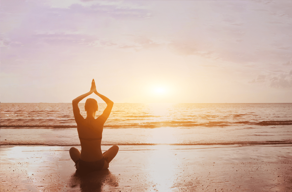 Mind-body medicine - woman doing sunset meditation on the beach