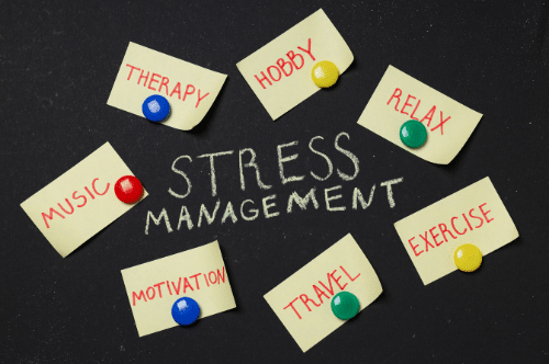 blackboard with "stress management" written on it. Words surrounded by post it notes reading "therapy," "hobby," relax," "exercise," "travel," "motivation," and "music."